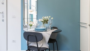 Un coin repas avec une table dressée pour deux personnes, agrémenté d’une nappe à rayures, d’assiettes bleues et d’un vase contenant des fleurs blanches.