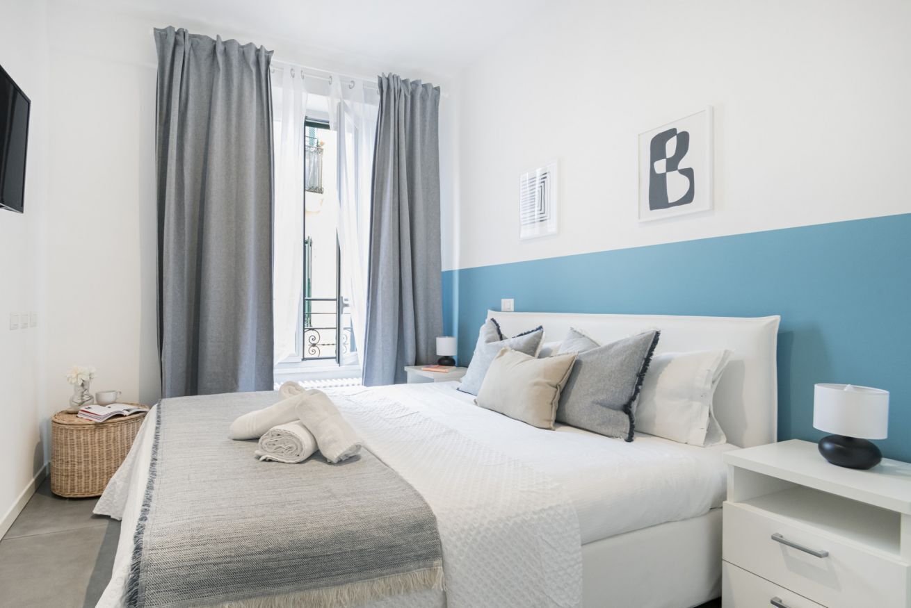 Un dormitorio ordenado con cama, mesita de noche y vistas al exterior.