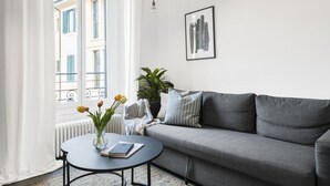 Un salon moderne avec un canapé gris, une table basse ronde sur laquelle se trouvent un livre et un vase, une plante en pot et un tableau encadré au mur.