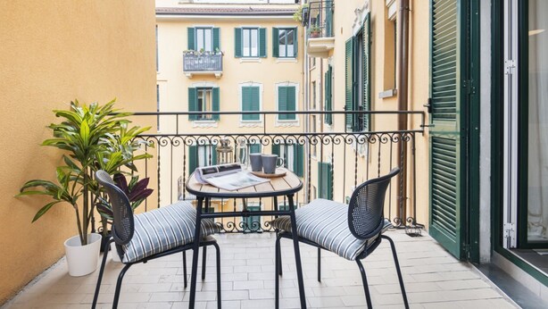 A small outdoor balcony with a round table and two chairs, surrounded by a metal railing.
