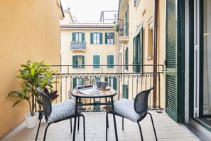 A small outdoor balcony with a round table and two chairs, surrounded by a metal railing.