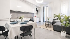 A modern kitchen with white cabinets, a dining table set with blue plates, and a grey sofa in the living area.