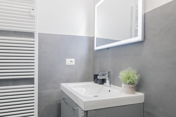 A modern bathroom with a white sink, a mirror, and a potted plant.