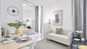 A modern living room with a sofa, a dining table with placemats, a plant, and a framed artwork on the wall.