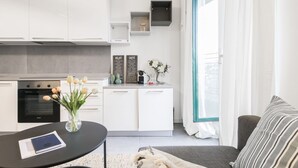 A modern kitchen with white cabinets, a black countertop, and a vase of tulips. There is a dining table with a book and a coffee machine. - Easylife - Beautiful flat in Porta Romana (Milano)
