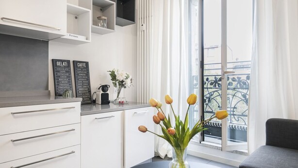 A modern kitchen with white cabinets, a black countertop, and a vase with tulips on a table. - Easylife - Beautiful flat in Porta Romana (Milano)