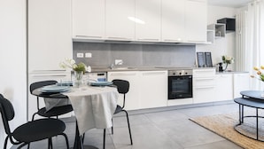 A modern kitchen with white cabinets, a dining table with chairs, and a small island with a sink. - Easylife - Beautiful flat in Porta Romana (Milano)