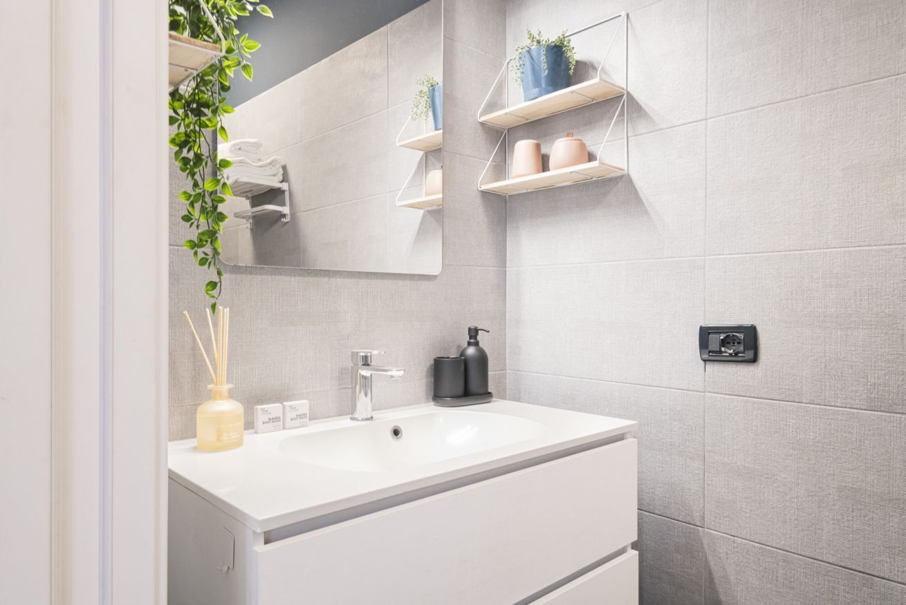 A modern bathroom with a white vanity, a large mirror, and built-in shelves with plants.