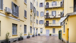 Une cour intérieure bordée de bâtiments jaunes, avec des unités de climatisation et des plantes en pot.