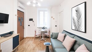 Un salon moderne avec un canapé, une table à manger et des chaises, un téléviseur fixé au mur et un tableau encadré.