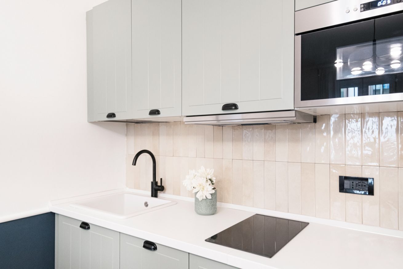 Une cuisine moderne avec des meubles de couleur gris clair, un plan de travail blanc, un robinet noir et un four en acier inoxydable.