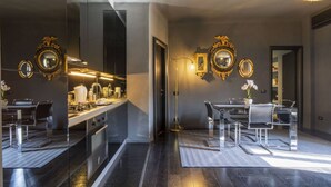 A modern kitchen with a central island, a dining area with a chandelier, and a hallway with mirrors and a potted plant.