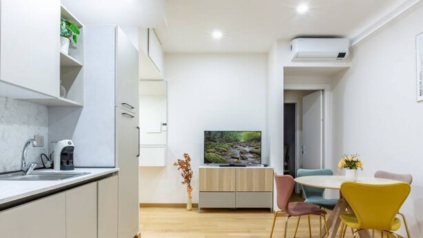 A modern kitchen with white cabinets, a built-in coffee machine, and a TV on a wooden stand. - Easylife - Cozy two-room apartment in Porta Venezia area (Milano)