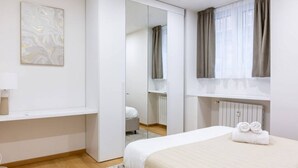 A modern bedroom with a bed, a wardrobe, a mirror, a radiator, and a window with curtains. - Easylife - Cozy two-room apartment in Porta Venezia area (Milano)