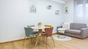 A modern living room with a round dining table, colorful chairs, a grey sofa, and a small white coffee table. - Easylife - Cozy two-room apartment in Porta Venezia area (Milano)
