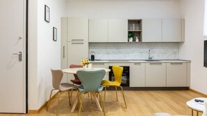 A modern kitchen with white cabinets, a marble countertop, and a dining area with a round table and colorful chairs.