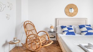 Une chambre à coucher comprenant un lit, un fauteuil à bascule, une table de chevet, une lampe et un mur orné d’un miroir rond.