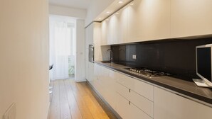 Moderni keittiö, jossa on valkoiset kaapit, musta työtaso ja sisäänrakennettu liesi.