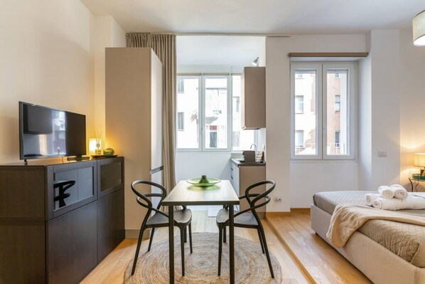 Habitación de hotel moderna con una cama, un escritorio con silla, televisión y vistas a la ciudad a través de amplias ventanas.
