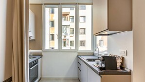 Eine kleine Küche mit Fenster, einer Kaffeemaschine und Blick auf ein Gebäude.