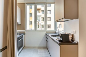 A compact kitchen with a window, a coffee machine, and a view of a building outside. - Easylife - Cozy studio close to the center (Milano)