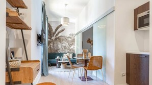 Et moderne køkken med træskabe, et spiseområde med et rundt bord og stole, og en stue med en sofa og en stor plante.