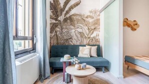 En moderne stue med en grøn sofa, et rundt sofabord og et stort vægmaleri med tropisk vegetation.
