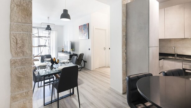 A modern kitchen with a large island, a dining area with a glass table, and a stone accent wall.