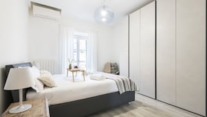 A modern bedroom with a bed, bedside table, lamp, and a view of the outside.