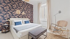 A bedroom with a bed, bedside table, bench, chair, and a window with curtains. - Easylife - Golden Navy Design apt Pta Venezia (Milano)