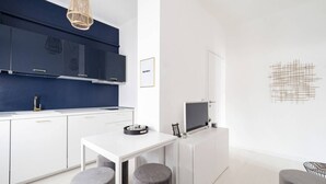 A modern kitchen with dark blue cabinets, a white countertop, and a dining area with a white table and grey stools. - Easylife - Golden Navy Design apt Pta Venezia (Milano)