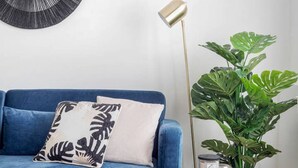 A blue sofa with a white and black pillow, a tall floor lamp, and a large green plant. - Easylife - Golden Navy Design apt Pta Venezia (Milano)