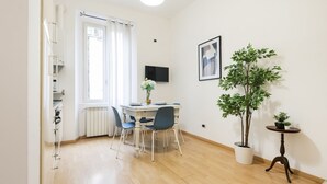 A compact living space with a dining area, a radiator, a TV mounted on the wall, and a potted plant. - Easylife - Comfortable three-room apartment in the heart of Milan (Milano)