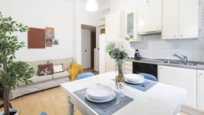 A modern kitchen with white cabinets, a dining table set with plates and cutlery, and a vase with flowers. - Easylife - Comfortable three-room apartment in the heart of Milan (Milano)