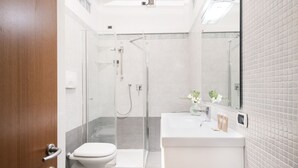 A modern bathroom with a glass-enclosed shower, a toilet, and a sink with a mirror. - Easylife - Comfortable three-room apartment in the heart of Milan (Milano)