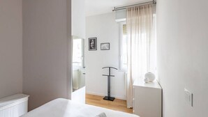 A minimalist bedroom with a large bed, a bedside table with a lamp, and a window with curtains. - Easylife - Sophisticated studio with balcony in the heart of Porta Venezia (Milano)