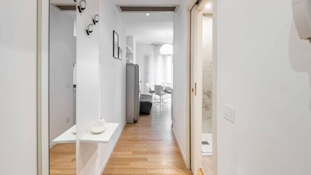A modern, well-lit hallway with a wooden floor, leading to a dining area with a table and chairs. - Easylife - Sophisticated studio with balcony in the heart of Porta Venezia (Milano)