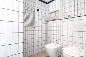 Un bagno moderno con piastrelle bianche, una vasca da bagno bianca, un lavabo e un water.