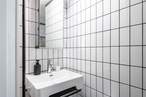 A bathroom with white tiles, a white sink, a black soap dispenser, and a mirror. - Easylife - Oasis of Style&Comfort in Porta Venezia (Milano)