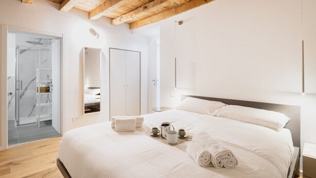 Une chambre moderne avec un plafond en bois, un grand lit avec du linge de lit blanc, une douche en verre et un dressing.