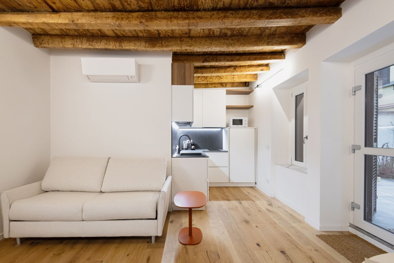 A modern living room with a sofa, a small table, and a kitchen area in the background.
