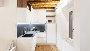 Une cuisine de taille réduite avec des meubles blancs, un évier noir et un plafond en bois.