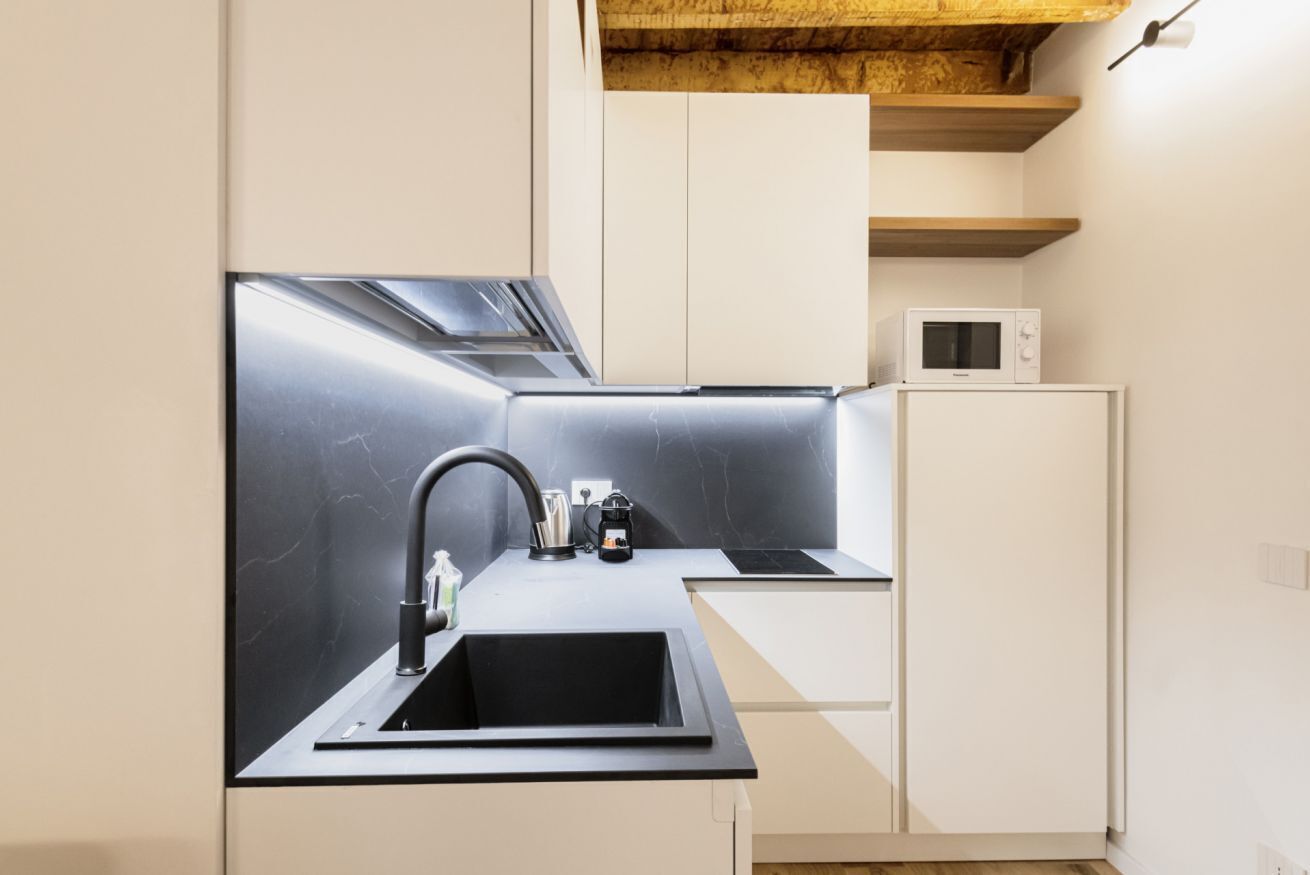 Une cuisine moderne avec un évier noir, des armoires blanches et un four à micro-ondes posé sur une armoire blanche.