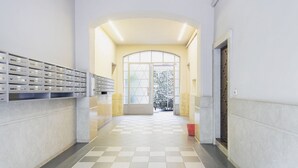 Un couloir doté d’un sol à carreaux, une porte vitrée donnant sur l’extérieur et une étagère avec des bacs de rangement.