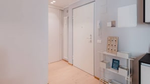 Moderni hotellihuone, jossa on puulattia, valkoinen ovi ja seinään integroitu hylly, jossa on kyltti.