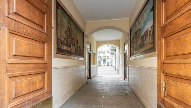 A corridor with wooden doors and paintings on the walls, leading to a building entrance.
