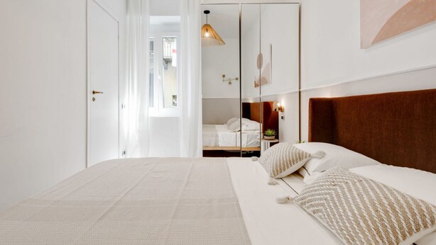 Un dormitorio moderno con una cama grande, un cabecero de madera, una mesita de noche con lámpara y un espejo.