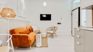 Una habitación moderna y bien iluminada con sofá, una silla, una mesita y un televisor montado en la pared.