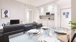 Een moderne woonkamer met een bank, een glazen eettafel gedekt voor vier personen en een keuken op de achtergrond.