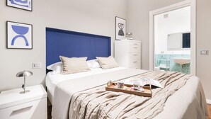 Een moderne slaapkamer met een groot bed, een nachtkastje, een kast en een badkamer zichtbaar door een geopende deur.